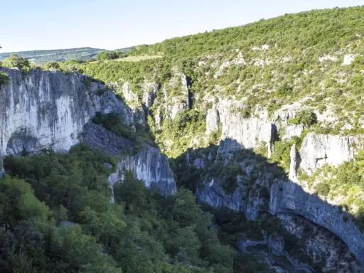 Vue plongeante sur les gorges d'Oppedette, falaises calcaires abruptes couvertes de végétation luxuriante sous un ciel bleu.
