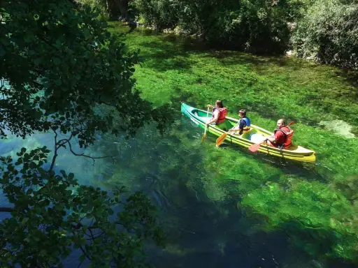 Trois personnes en canoë sur la Durance, profitant d'une baignade rafraîchissante dans des eaux turquoise et verdoyantes.