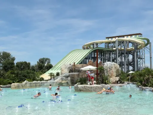 Ambiance estivale dans un parc aquatique Vaucluse. Des familles profitent de la piscine à bouées, sous les imposants toboggans verts et blancs.