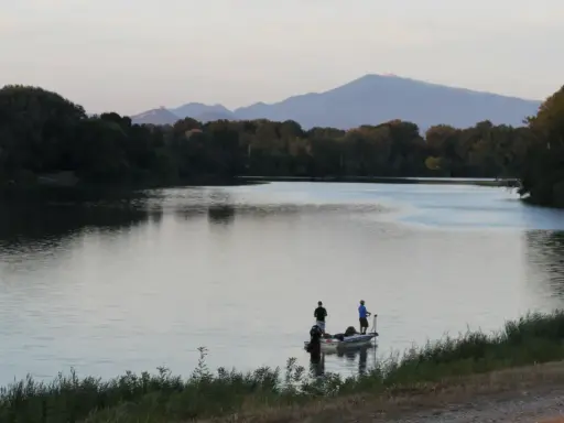 Deux pêcheurs sur un bateau profitent du calme du plan d'eau du Revestidou, avec des montagnes en arrière-plan.