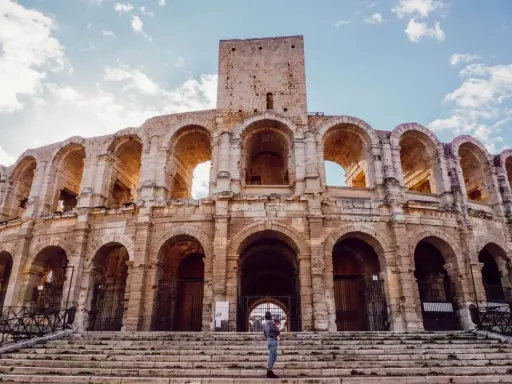 Visiter Arles : une personne tient un bébé sur les marches de l'amphithéâtre romain, sous un ciel bleu et nuageux.