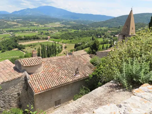Vue panoramique d'un village provençal avec ses toits de tuiles, sa campagne verdoyante et ses montagnes. Une belle activité gratuite Vaucluse pour s'évader.
