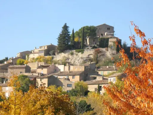 Village de Joucas, France, en automne. Les maisons en pierre s'étagent sur la colline, entourées d'arbres aux couleurs flamboyantes.