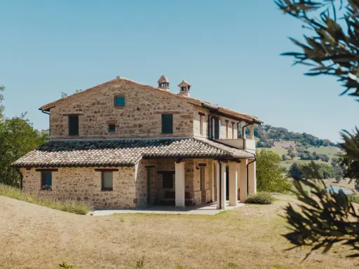 Un mas en pierre typique du sud de la France, niché dans des collines verdoyantes sous un ciel bleu éclatant.