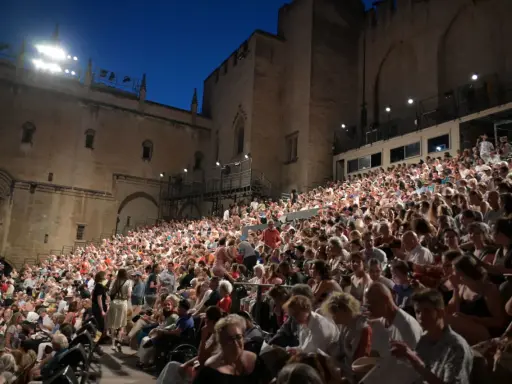 Foule nombreuse assise sur des gradins, devant un palais, pour la Fête de la Musique à Avignon.