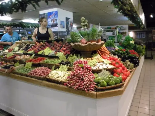 Un étal coloré au marché d'Avignon présente une abondance de fruits et légumes frais : pêches, tomates, haricots verts, radis, aubergines, et plus encore.
