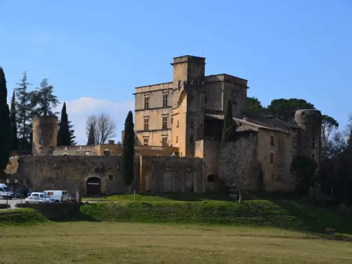 Le majestueux **Château de Lourmarin** se dresse sur une colline, ses pierres ocres baignées de soleil sous un ciel bleu. Des cyprès élancés l'entourent.