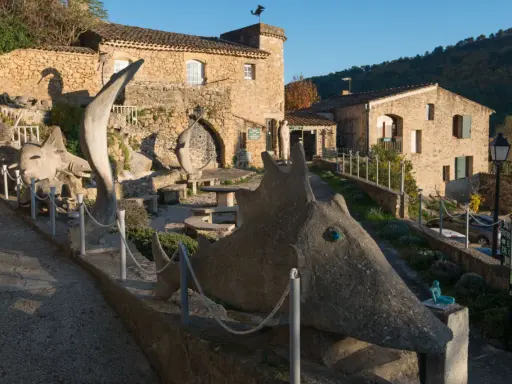 Sculptures étranges devant le musée extraordinaire Ansouis. Un chemin serpente entre des créatures de pierre et des bâtiments en pierre.