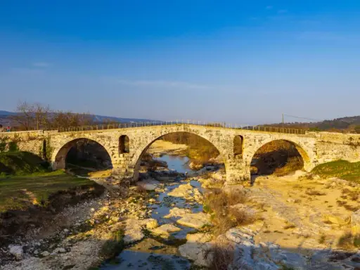 Le **pont Julien**, un ancien pont de pierre à trois arches, enjambe une rivière asséchée bordée de rochers et de végétation.