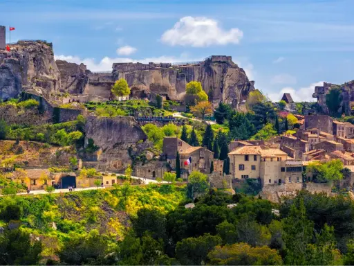 Vue panoramique de la route des villages perchés, avec un château en ruines dominant des maisons en pierre et une végétation luxuriante sous un ciel bleu.