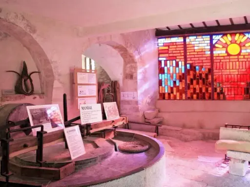 Dans le musée du vitrail Gordes, une roue de moulin ancienne côtoie un vitrail éclatant de soleil et de couleurs chaudes.