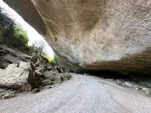 Le chemin menant au fort de Buoux serpente sous un immense surplomb rocheux, offrant un aperçu de la nature sauvage.