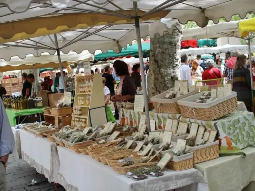 Ambiance animée au marché de Lourmarin, avec des étals de produits locaux, herbes aromatiques et bouteilles d'huile d'olive.