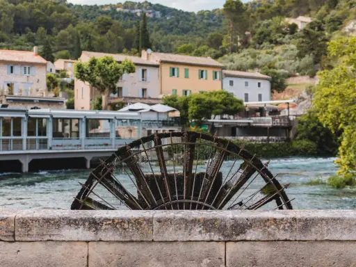 Roue à aubes rouillée sur la Sorgue, avec des maisons provençales en arrière-plan. Le **gouffre de Fontaine-de-Vaucluse** est une source d'eau d'une beauté saisissante.