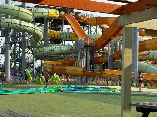 Des toboggans colorés et sinueux dominent le parc aquatique de Monteux. Des visiteurs se préparent à glisser, certains portant des bouées vertes.