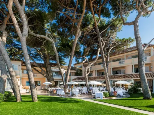 Un magnifique cheval blanc se promène dans un jardin luxuriant en Provence, près d'un hôtel de luxe avec terrasse.