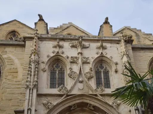 Détail architectural d'une cathédrale, un joyau du tourisme à Carpentras. Gargouilles et fenêtres gothiques sous un ciel couvert.