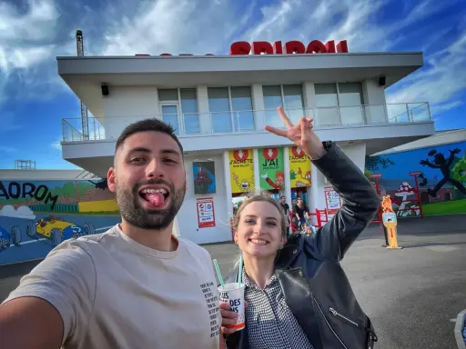 Un couple s'amuse devant le parc Spirou. La femme fait un signe de paix. Combien de temps pour faire le parc Spirou ? Une journée entière !