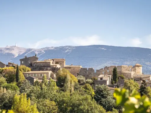 Vue d'un faucon village perché sur une colline, avec une église et des ruines médiévales. Le Mont Ventoux domine l'horizon.