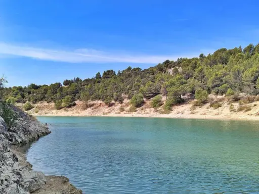Le lac du Paty, aux eaux turquoise, est bordé de rochers et de collines verdoyantes sous un ciel bleu.