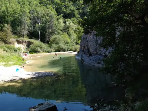 Des baigneurs profitent d'une rivière aux eaux claires près du rocher des abeilles, certains escaladent la paroi rocheuse.