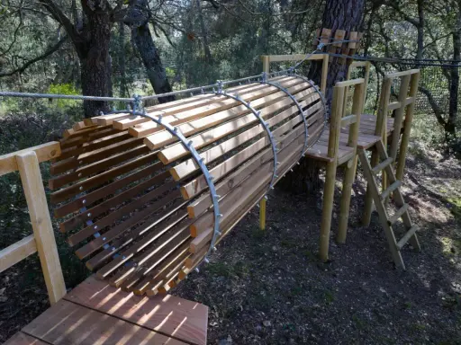 Un tunnel en bois et métal, partie d'un parcours aventure dans la forêt enchantée Venasque. Une échelle mène à une plateforme.
