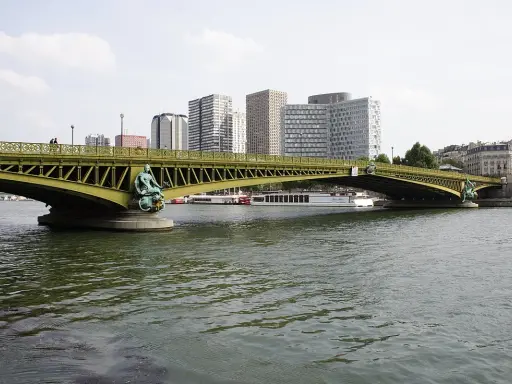 Le pont Mirabeau, avec ses statues de sirènes, enjambe la Seine, bordée par des immeubles modernes et des péniches.