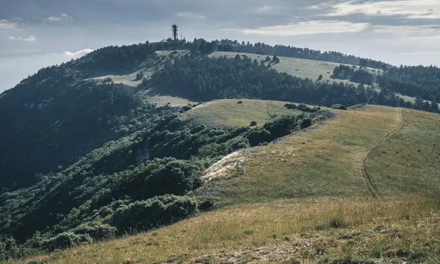 Vue panoramique du Moure Negre, avec une tour de télécommunication au sommet, des collines verdoyantes et un sentier sinueux.