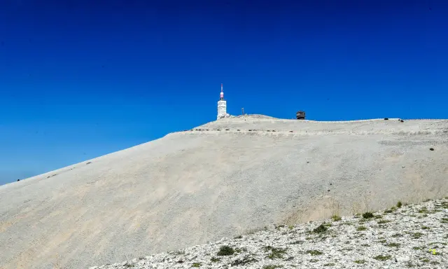 Le Mont Ventoux, sommet aride sous un ciel bleu intense, dominé par une tour de télécommunication.