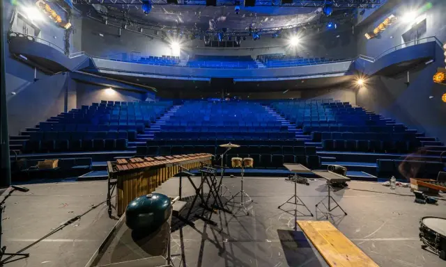 Scène de concert vide avec sièges bleus, marimba, batterie et projecteur, prête pour un spectacle à la Scala Provence.