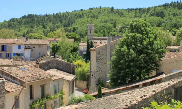 Vue d'un village provençal avec ses toits de tuiles, un clocher et une colline boisée. On imagine le marché de Cereste animé sous le soleil.