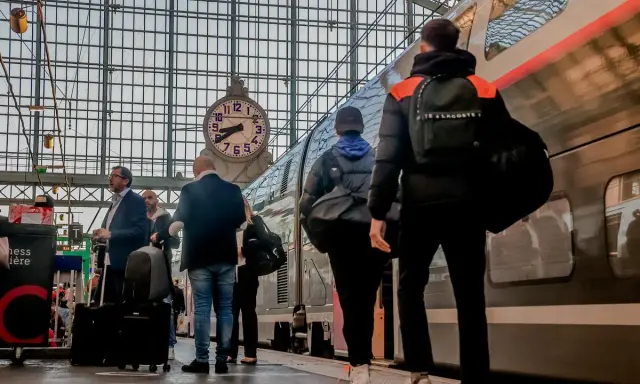 Voyageurs attendant le train pour Apt, sous une grande horloge dans une gare.