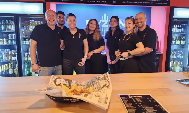 L'équipe du bar Elyzion, souriante, pose devant les réfrigérateurs. Sur le comptoir, des nachos et un menu.