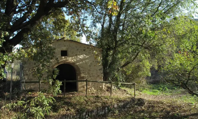 Ancienne bâtisse en pierre avec une arche, entourée d'arbres feuillus et d'une clôture en bois. Un lieu paisible dans le parc de l'arbousière.