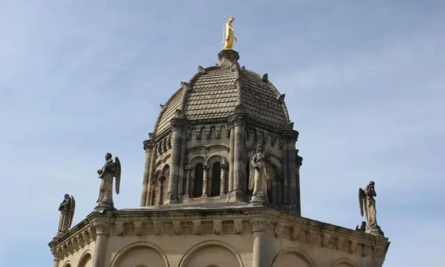 Dôme de Notre Dame de Provence, orné de statues d'anges et surmonté d'une Vierge dorée, sous un ciel bleu.