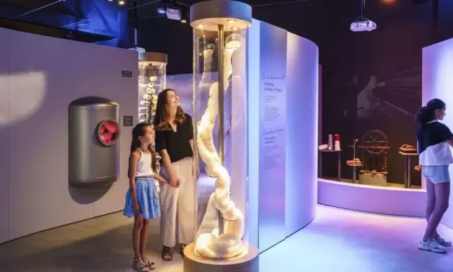 Une mère et sa fille découvrent la filaventure dans un musée interactif, fascinées par une colonne de fibres.