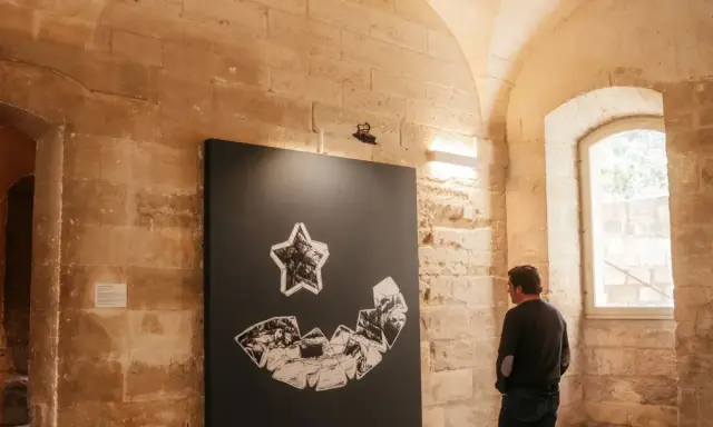 Un homme admire une œuvre d'art abstraite lors d'une expo Avignon. La pièce représente une étoile au-dessus d'une forme souriante composée de fragments.