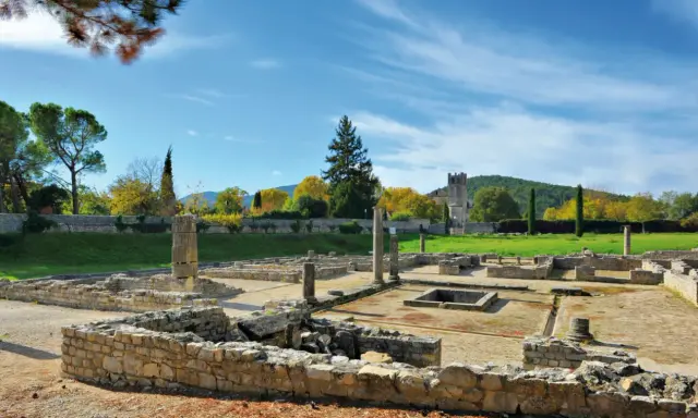 Vestiges romains ensoleillés, parfaits pour visiter Vaison-la-Romaine. Ruines antiques, colonnes et un clocher médiéval en arrière-plan.