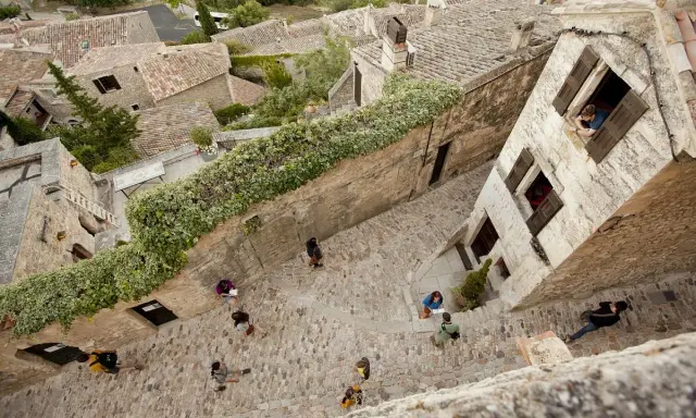 Vue plongeante d'une ruelle pavée bordée de maisons anciennes. Des touristes explorent ce village pittoresque, un peu comme un scad Lacoste, profitant de l'atmosphère paisible.
