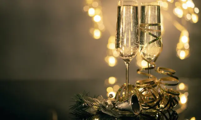 Deux flûtes de champagne pétillant, décorées de rubans dorés, prêtes pour le nouvel an à Avignon. Lumières festives en arrière-plan.