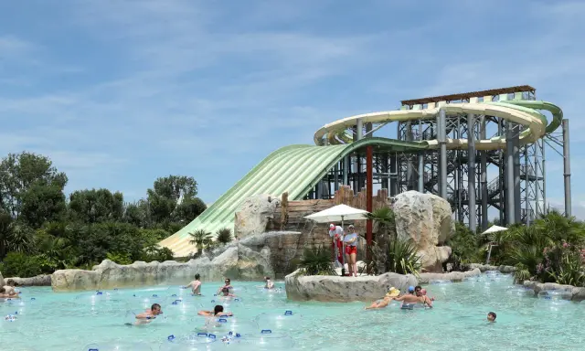 Ambiance estivale dans un parc aquatique Vaucluse. Des familles profitent de la piscine à bouées, sous les imposants toboggans verts et blancs.