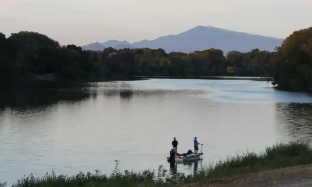 Deux pêcheurs sur un bateau profitent du calme du plan d'eau du Revestidou, avec des montagnes en arrière-plan.