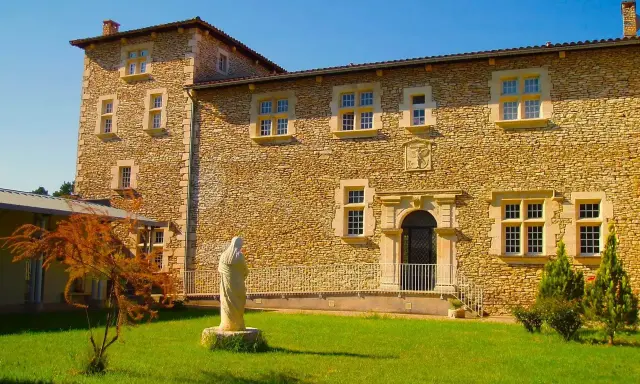 Statue de la Vierge devant la façade en pierre de la blauvac abbaye, sous un ciel bleu éclatant.