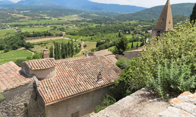 Vue panoramique d'un village provençal avec ses toits de tuiles, sa campagne verdoyante et ses montagnes. Une belle activité gratuite Vaucluse pour s'évader.