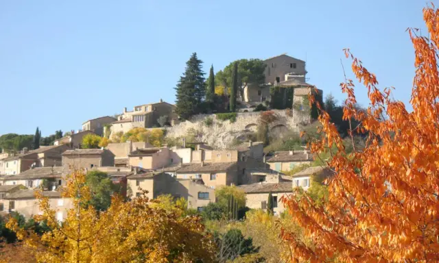 Village de Joucas, France, en automne. Les maisons en pierre s'étagent sur la colline, entourées d'arbres aux couleurs flamboyantes.