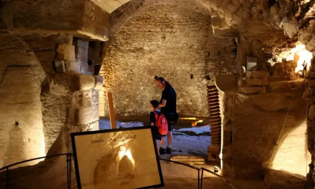 Un homme et un enfant explorent les caves du palais saint-firmin, un lieu historique aux voûtes de pierre.