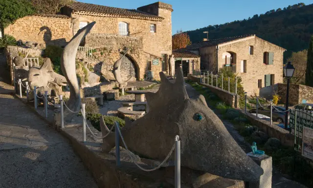 Sculptures étranges devant le musée extraordinaire Ansouis. Un chemin serpente entre des créatures de pierre et des bâtiments en pierre.