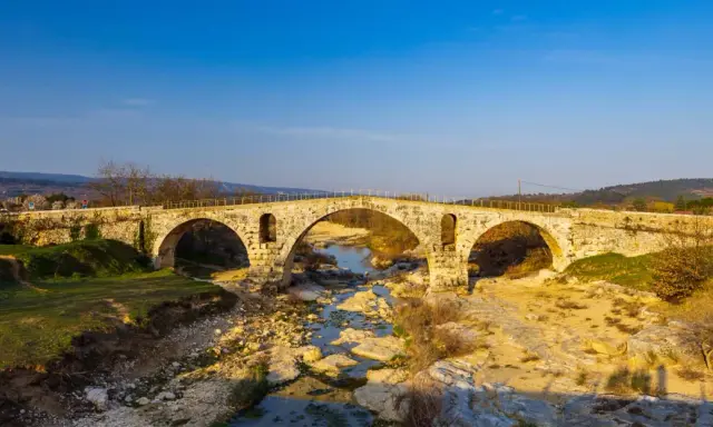 Le **pont Julien**, un ancien pont de pierre à trois arches, enjambe une rivière asséchée bordée de rochers et de végétation.