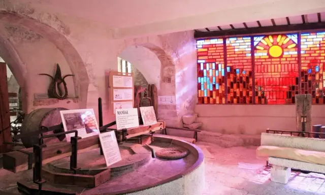 Dans le musée du vitrail Gordes, une roue de moulin ancienne côtoie un vitrail éclatant de soleil et de couleurs chaudes.