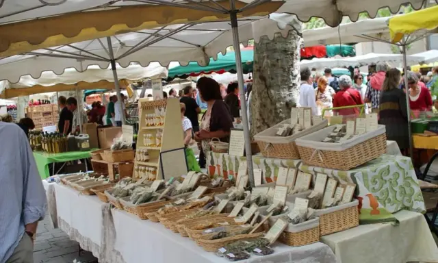 Ambiance animée au marché de Lourmarin, avec des étals de produits locaux, herbes aromatiques et bouteilles d'huile d'olive.